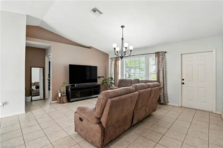 Living area with light tile patterned floors, a chandelier, and vaulted ceiling
