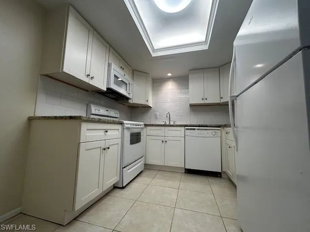 Kitchen with white appliances, white cabinets, and light tile patterned floors