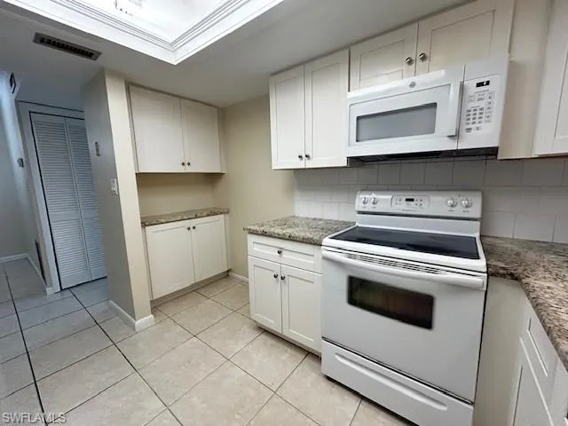 Kitchen with white appliances, white cabinetry, light tile patterned flooring, backsplash, and light stone countertops