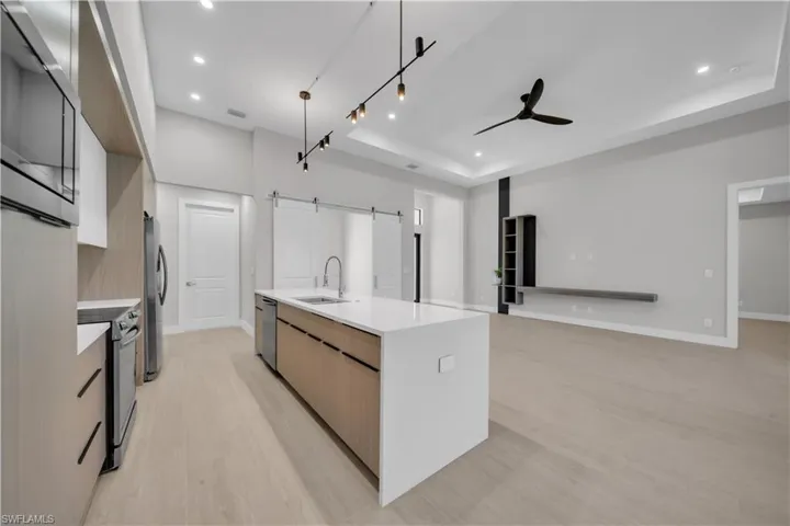 Kitchen featuring two tone cabinets, stainless steel appliances, a barn door, decorative light fixtures, and modern cabinets