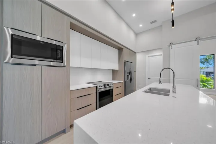Two tone kitchen featuring modern cabinets, two tone cabinetry, light stone counters, stainless steel appliances, and a barn door