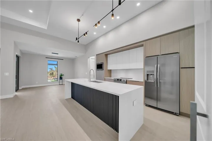 Kitchen featuring stainless steel appliances, a kitchen island with sink, dual tone cabinetry, light stone counters, and light wood-type flooring