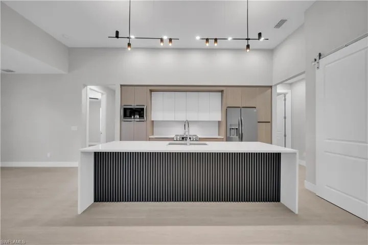 Two tone kitchen with a barn door, a large island, stainless steel appliances, light stone countertops, and two tone cabinets