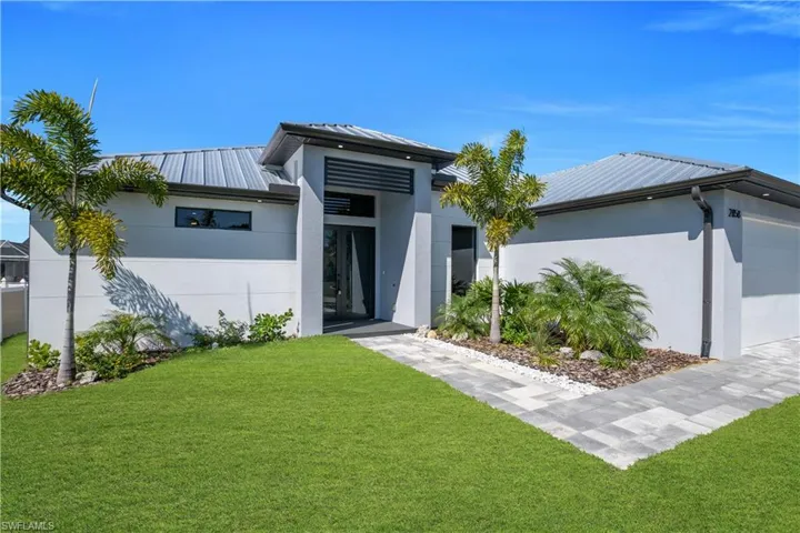 View of front of home featuring an attached garage, stucco siding, a front yard, and a standing seam roof