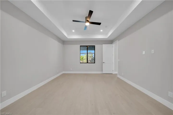 Empty room featuring a ceiling fan, light wood-type flooring, a raised ceiling, and recessed lighting