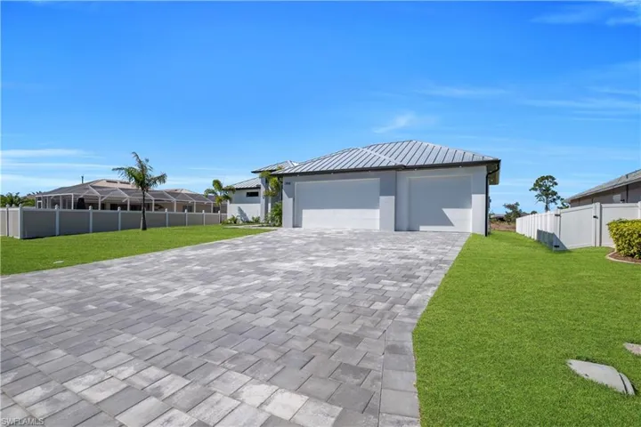 View of front facade featuring decorative driveway, a standing seam roof, a gate, and a garage