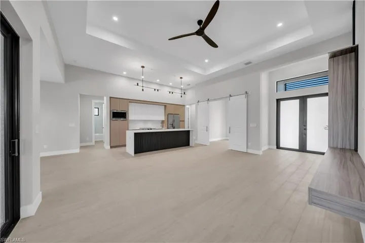 Unfurnished living room with a barn door, ceiling fan, a high tray ceiling, light wood finished floors, and recessed lighting