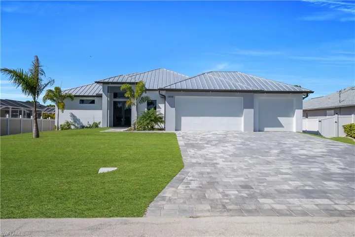 View of front of home featuring a standing seam roof, an attached garage, decorative driveway, stucco siding, and a gate