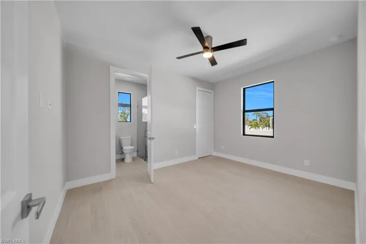 Unfurnished bedroom with light wood-type flooring, ceiling fan, and ensuite bathroom