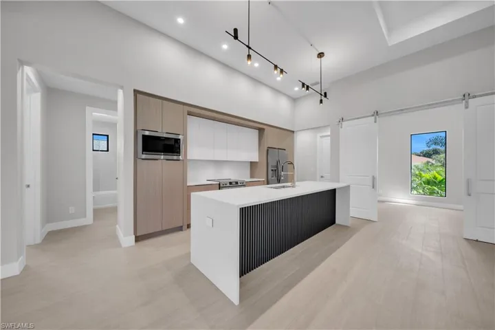 Kitchen with two tone color scheme, modern cabinets, an island with sink, a barn door, and stainless steel appliances