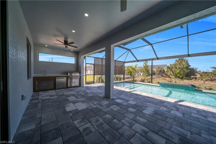 Outdoor pool featuring an outdoor kitchen, a sunroom, glass enclosure, and a patio area