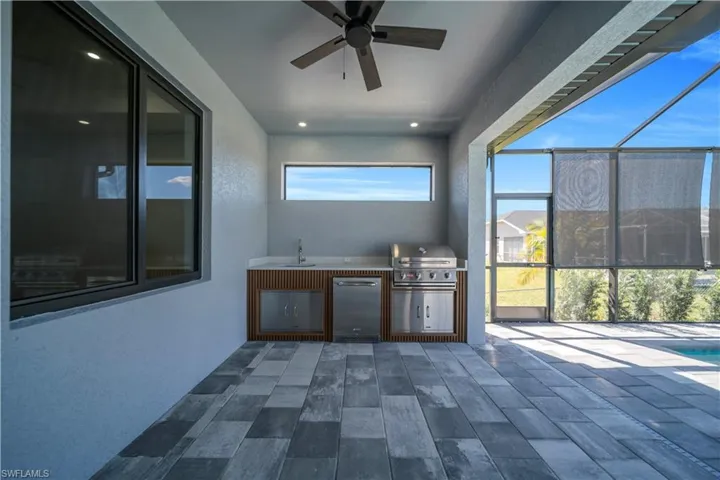 View of patio featuring glass enclosure, exterior kitchen, a sunroom, ceiling fan, and an outdoor pool