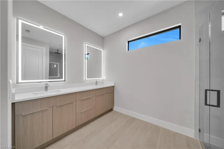 Full bath featuring double vanity, light wood finished floors, and a stall shower