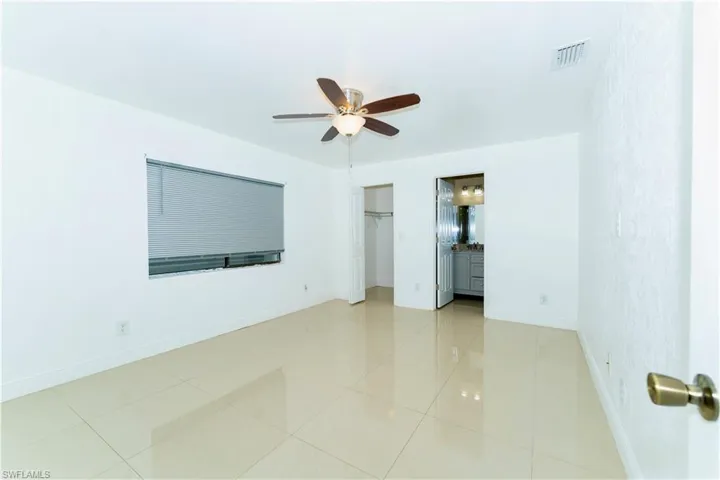 Unfurnished bedroom featuring a closet, ensuite bathroom, ceiling fan, and light tile patterned floors