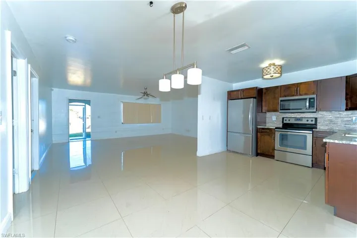 Kitchen featuring appliances with stainless steel finishes, hanging light fixtures, a ceiling fan, light stone counters, and backsplash