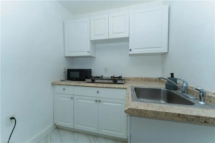 Kitchen featuring white cabinetry, light marble finish floors, black microwave, and light countertops