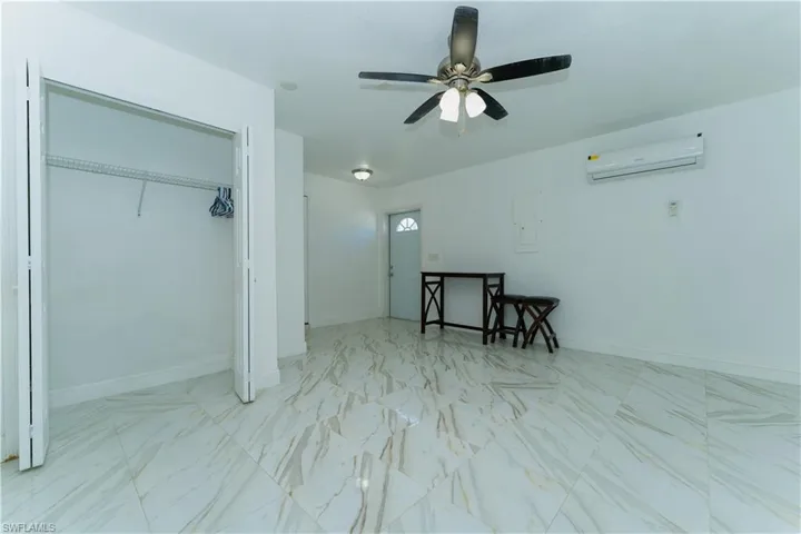 Bedroom with light marble finish floors, a closet, a wall unit AC, ceiling fan, and electric panel