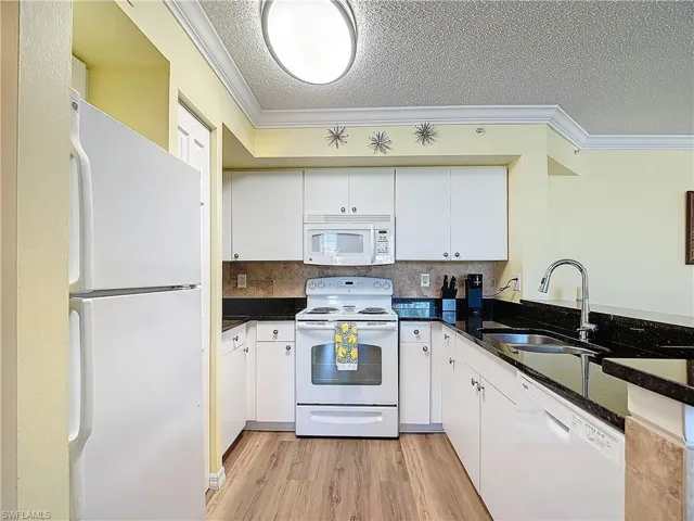 Kitchen featuring sink, crown molding, light wood-type flooring, and white appliances