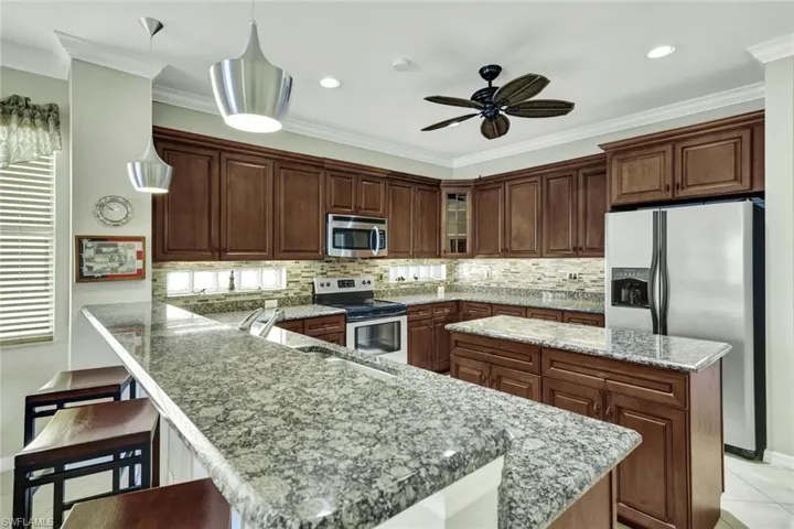 Kitchen with appliances with stainless steel finishes, a kitchen bar, a center island, hanging light fixtures, and light stone counters