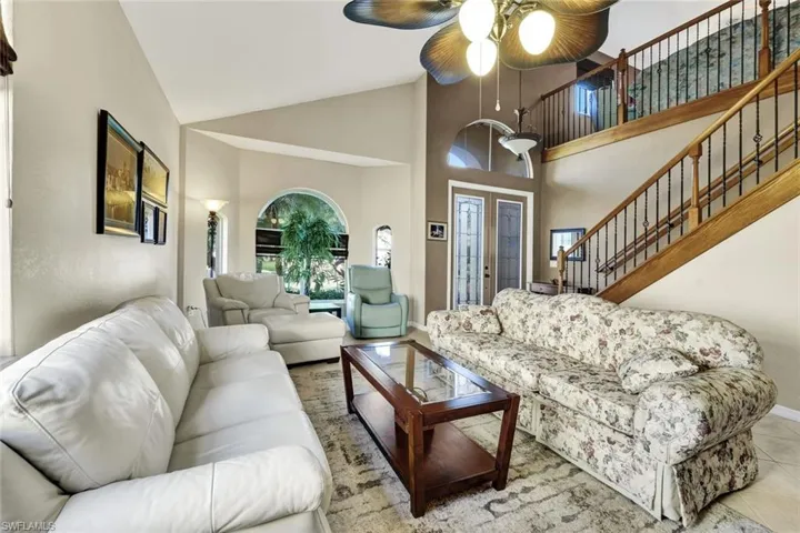 Living room with lofted ceiling, light tile patterned floors, and ceiling fan