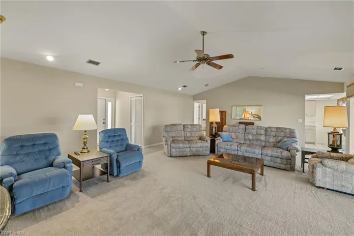 Carpeted living room with ceiling fan and lofted ceiling