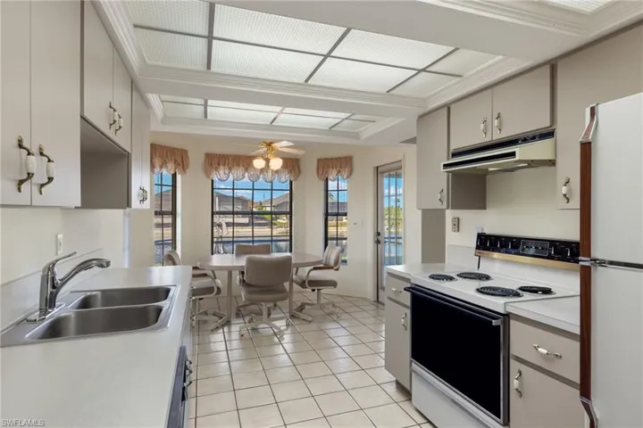 Kitchen featuring sink, white appliances, light tile patterned floors, ornamental molding, and ceiling fan