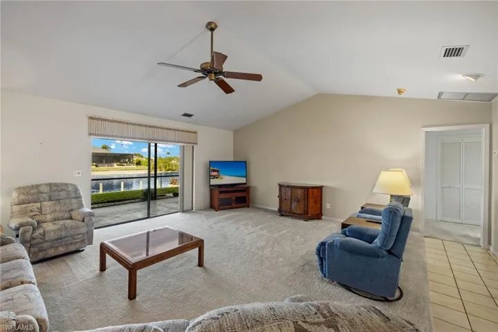 Carpeted living room featuring ceiling fan and vaulted ceiling