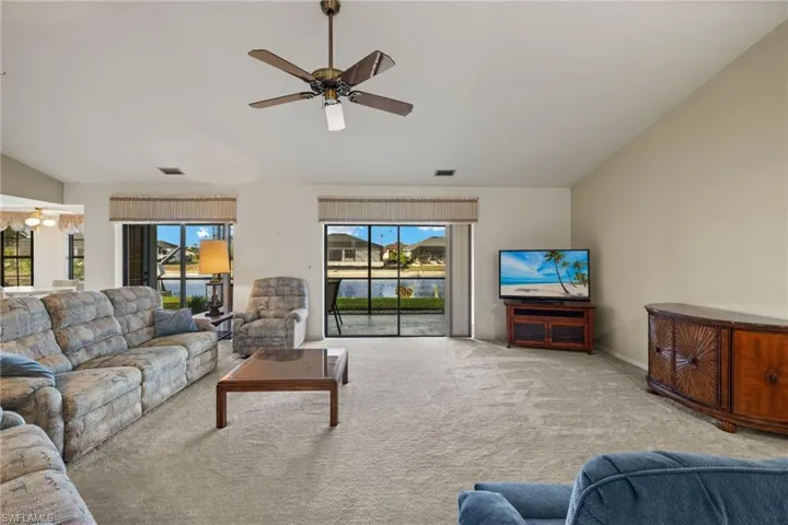 Carpeted living room with ceiling fan and vaulted ceiling