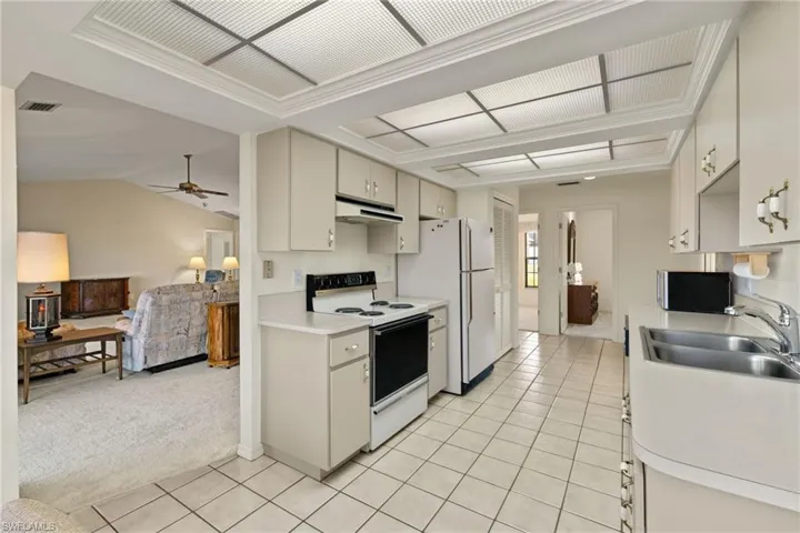 Kitchen with lofted ceiling, sink, white appliances, ceiling fan, and light colored carpet