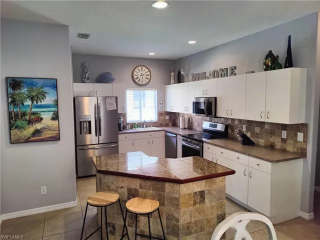 Kitchen featuring appliances with stainless steel finishes, backsplash, a kitchen bar, sink, and light tile floors