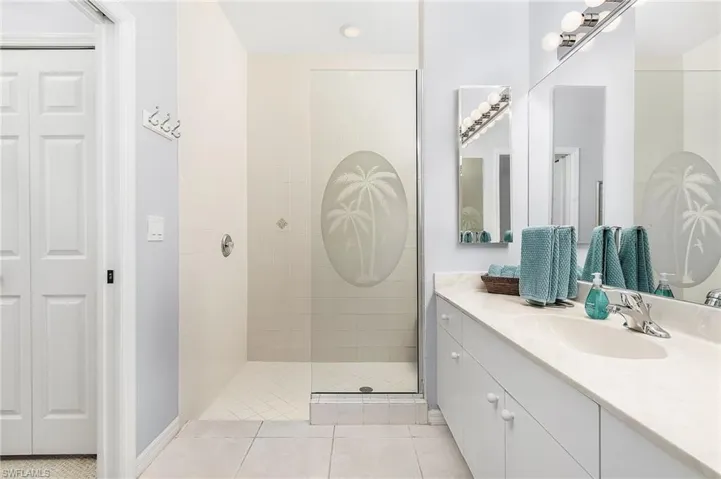 Bathroom with tiled shower, vanity with extensive cabinet space, and tile flooring