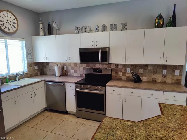 Kitchen with appliances with stainless steel finishes, white cabinetry, sink, and backsplash