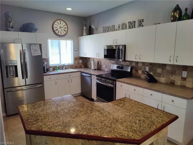 Kitchen featuring tile flooring, backsplash, sink, white cabinets, and appliances with stainless steel finishes