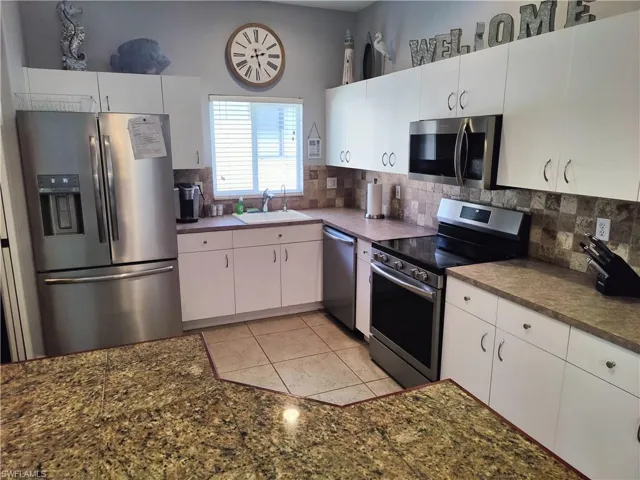 Kitchen with stainless steel appliances, white cabinets, sink, tasteful backsplash, and light tile flooring