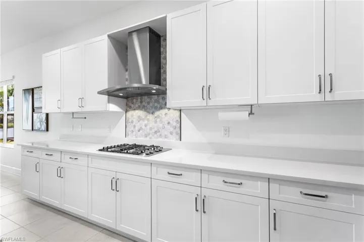 Kitchen with white cabinets, wall chimney exhaust hood, light tile patterned floors, and stainless steel gas stovetop