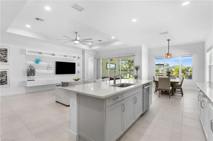 Kitchen featuring a raised ceiling, pendant lighting, recessed lighting, open floor plan, and a kitchen island with sink
