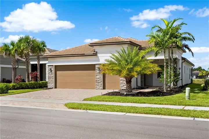 View of front facade with a front lawn, a garage, stone siding, decorative driveway, and stucco siding