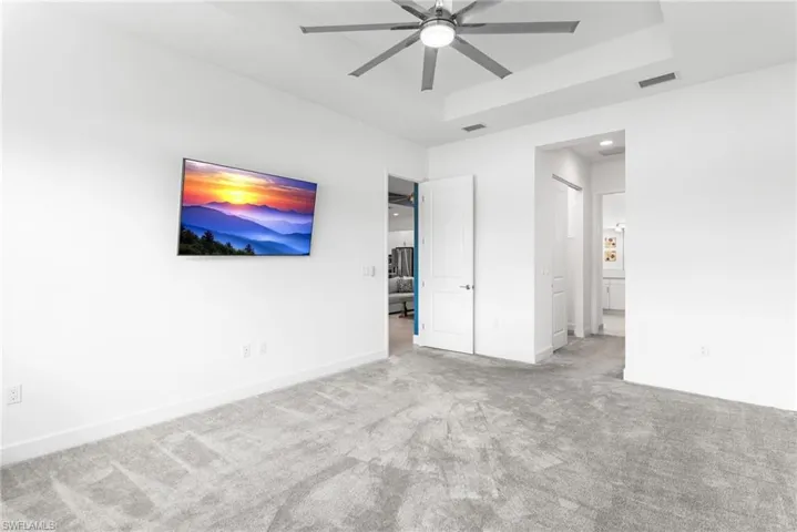 Unfurnished bedroom with carpet, ensuite bath, a raised ceiling, and a ceiling fan