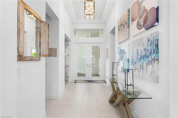 Entryway featuring french doors, healthy amount of natural light, light tile patterned floors, a chandelier, and a towering ceiling