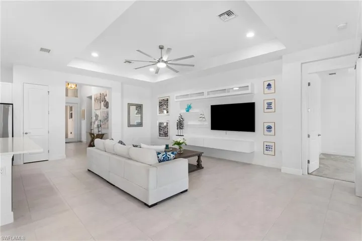 Living area with a tray ceiling, a ceiling fan, recessed lighting, and light tile patterned floors