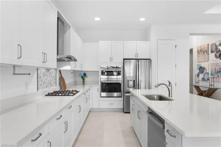 Kitchen with white cabinetry, stainless steel appliances, a center island with sink, wall chimney exhaust hood, and recessed lighting