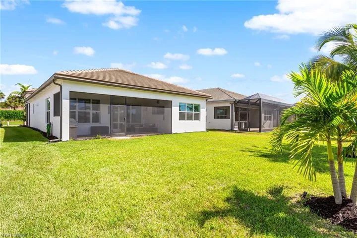 Rear view of property featuring stucco siding, a sunroom, a yard, and a lanai