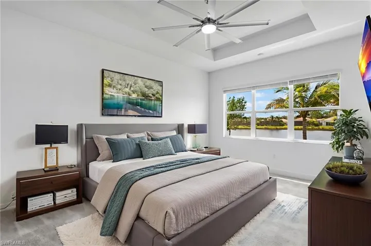 Carpeted bedroom featuring a raised ceiling and a ceiling fan