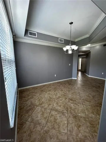 Unfurnished room with a chandelier, ornamental molding, a tray ceiling, baseboards, and tile patterned flooring