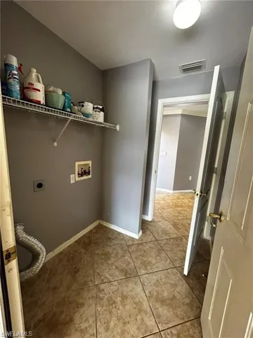 Clothes washing area with hookup for a washing machine, hookup for an electric dryer, tile patterned flooring, and baseboards