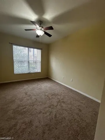 Carpeted empty room with a ceiling fan and baseboards