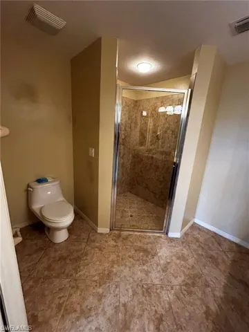 Bathroom featuring a shower stall, toilet, baseboards, and tile patterned flooring
