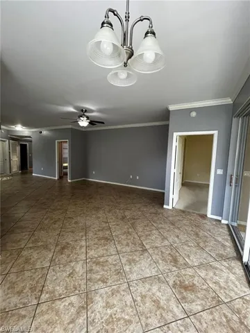Spare room with crown molding, a ceiling fan, tile patterned flooring, baseboards, and a chandelier