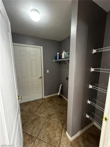 Clothes washing area featuring tile patterned flooring, baseboards, and hookup for an electric dryer
