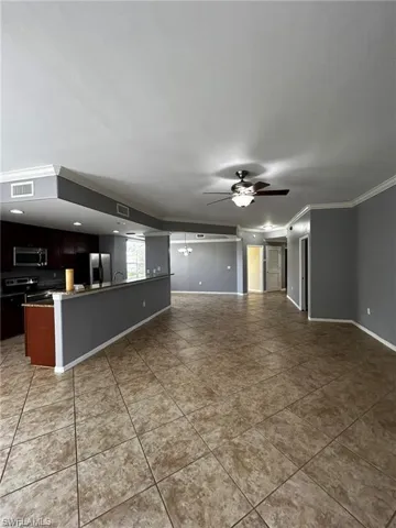 Unfurnished living room with ceiling fan, crown molding, baseboards, and tile patterned flooring